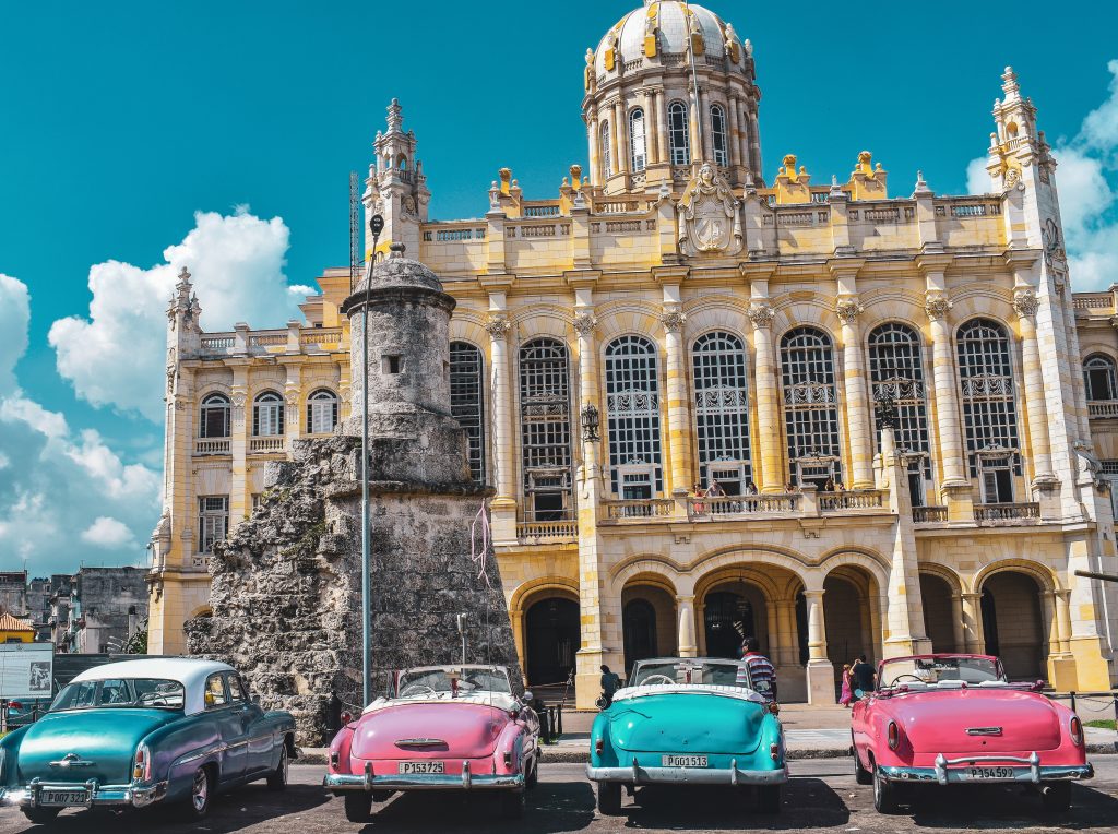 travel to cuba as an American. Old colorful american cars in front of an old building in havana. 