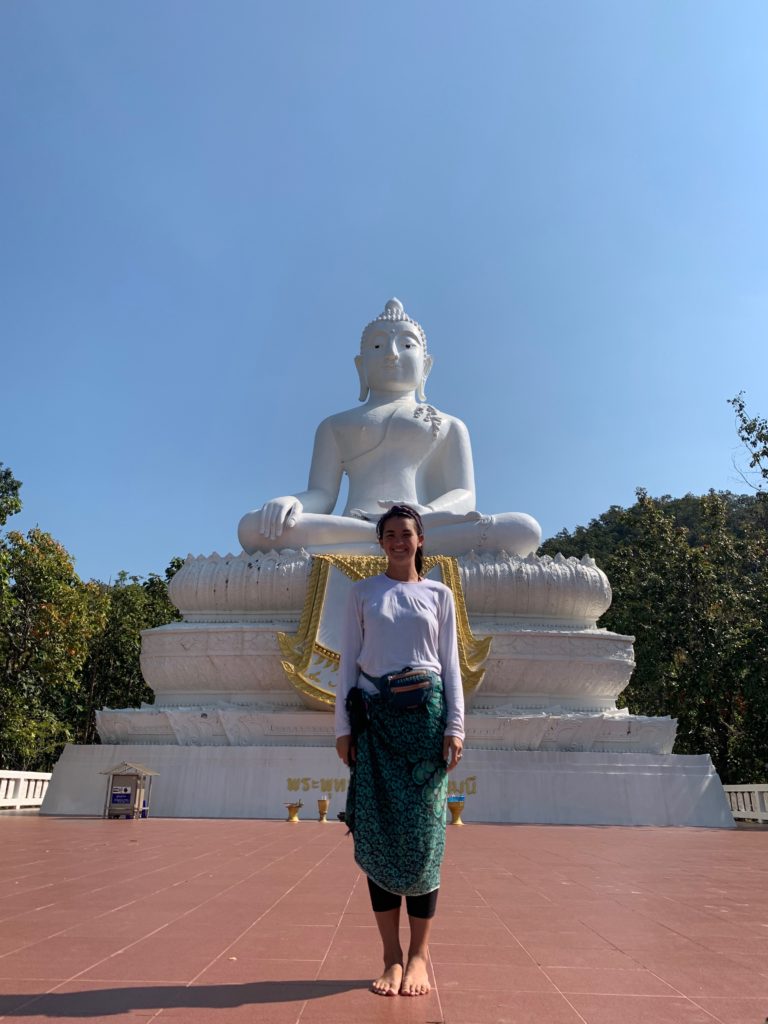 woman in green sarong with back to large white buddha statue. 