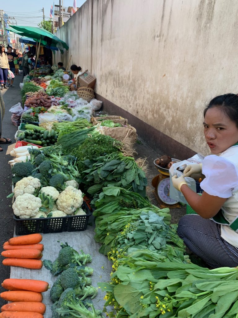 woman selling green vegetables on the side of the street 