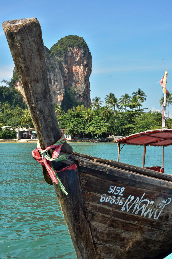 Thai boat on bright blue water with rocky mountains behind it. 