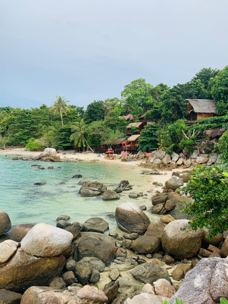 beach bungalows on yellow sand beach surrounded by lush jungle and rocks. 