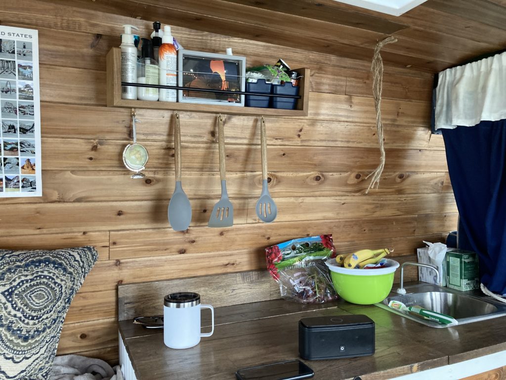 inside of a converted camper van. wooden countertop with fruit and other kitchen item on top. 