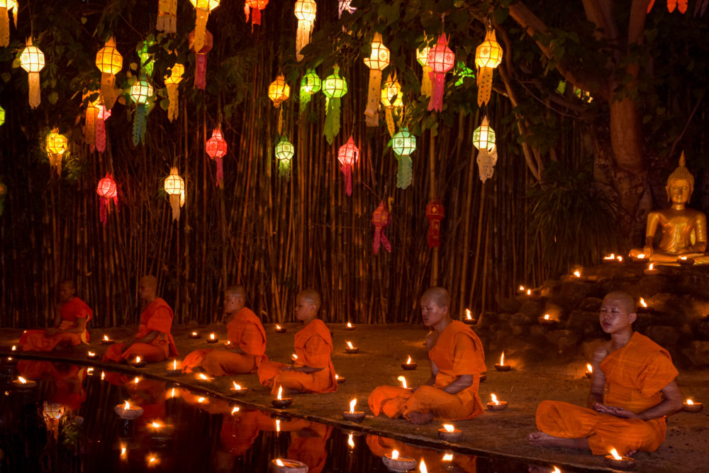 Orange robed monks sit by a lake lit by candles. Cultural travel 