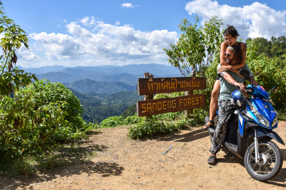 couple riding a blue motorbike overlooking a massive green forest. Cultural travel 