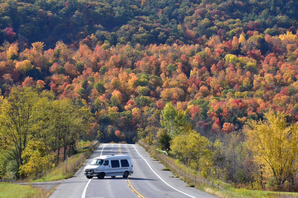 van sitting in the roadway with bright colorful fall foliage behind it. Budget USA Road trip 