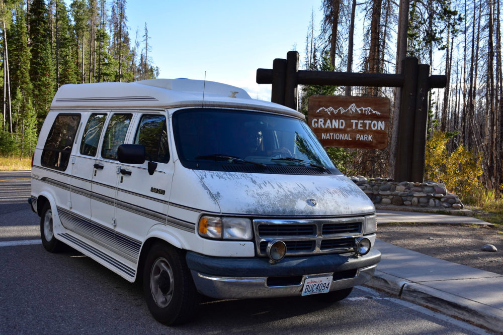 older white van sitting by wooden sign that says "Grand Teton National Park"