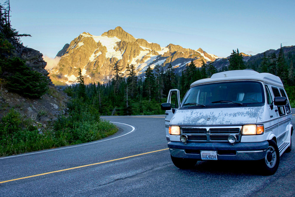 white van with doors open on a highway with snow capped mountains in the background. benefits of van life 