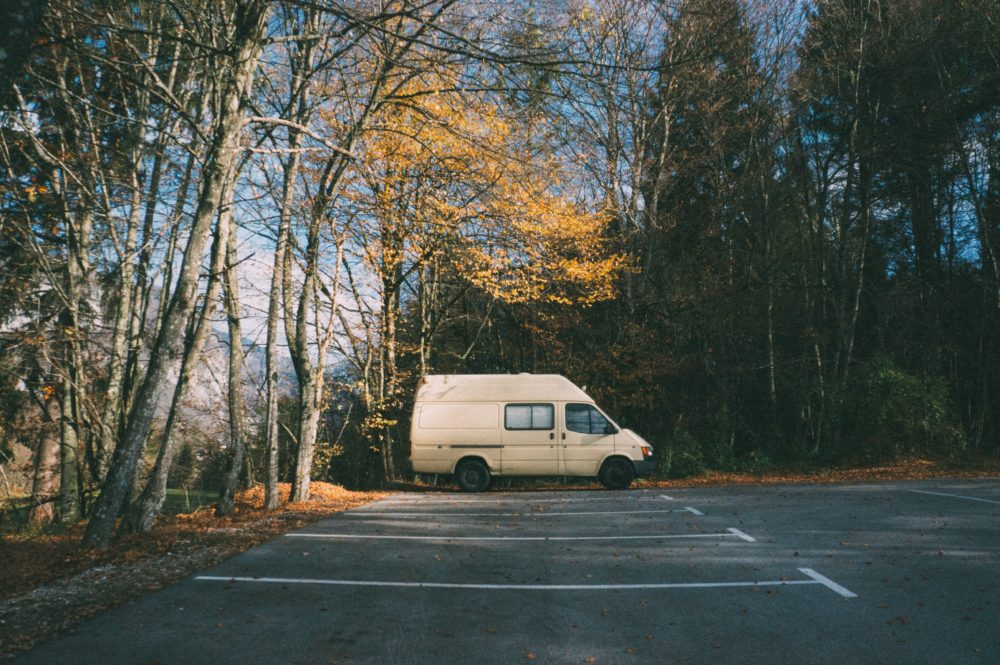 beige sprinter van sitting in a parking lot with golden leaves above it. reasons not to buy a sprinter for van life 