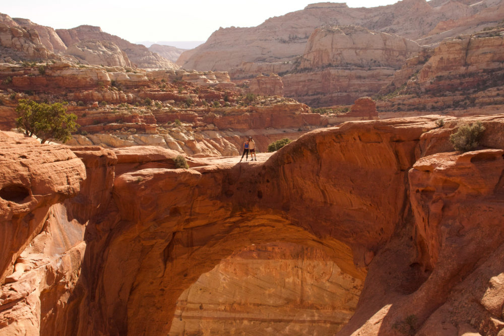 couple standing on ledge of arch at capitol reef national park 