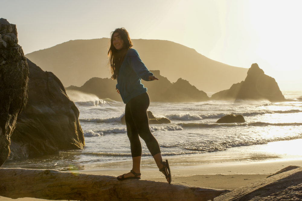 girl walking on a log brightly lit by the golden sunset on the beach. 