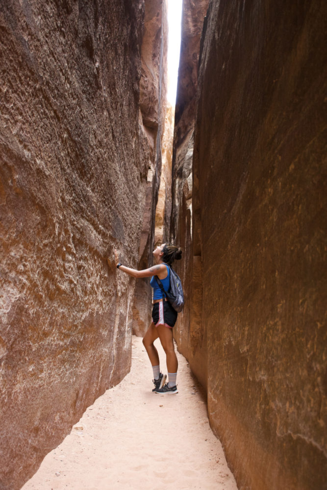 Woman standing in between two massive rock slabs looking upwards. 
