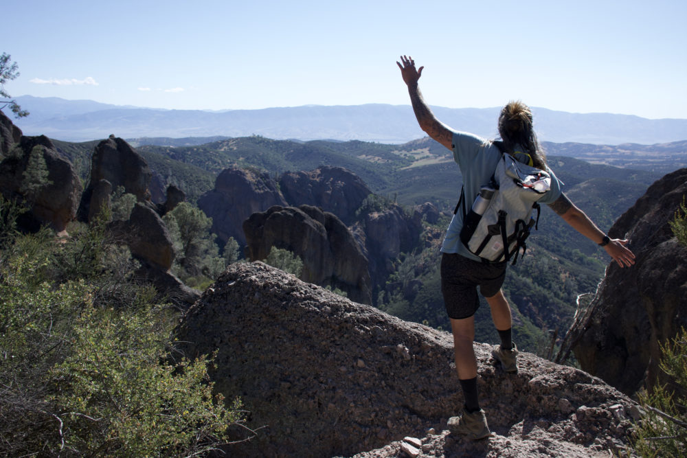 man balancing while walking across a ledge overlooking a scenic view. 