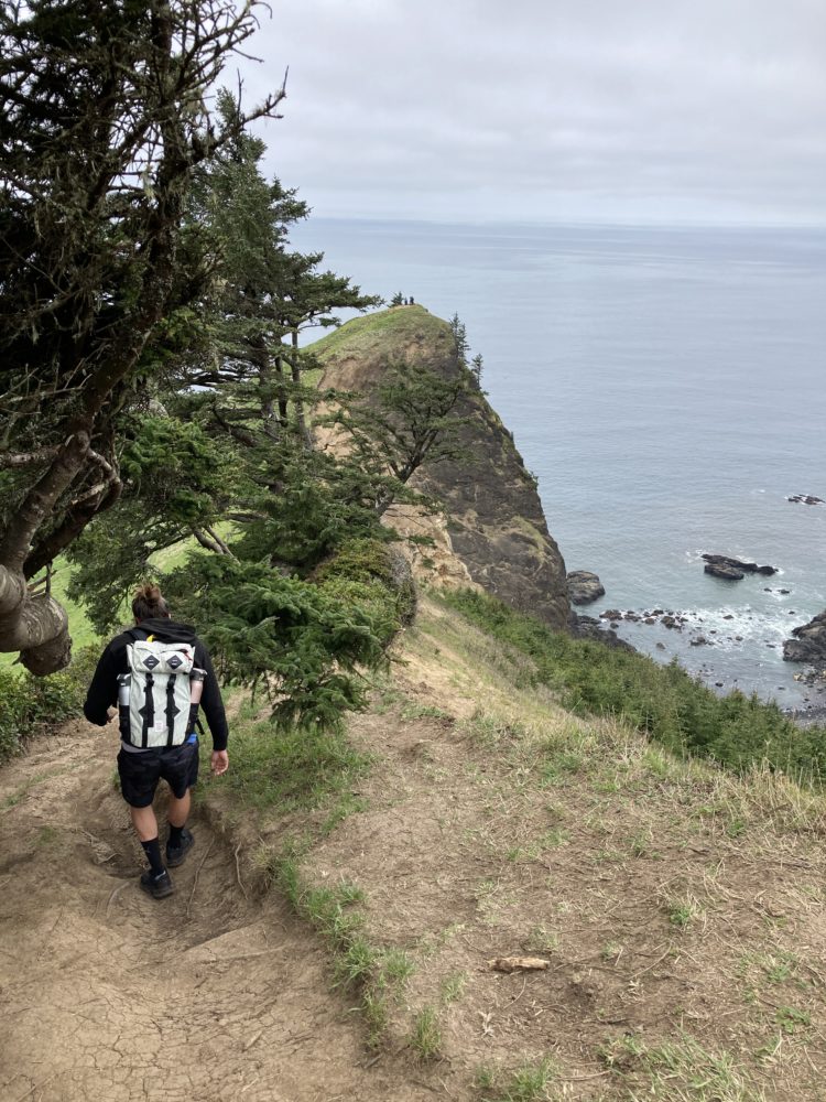 man walking on cliffside path to green knoll. 
