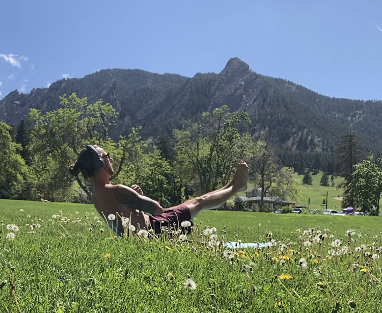 man working out in a green field in front of the mountains. 