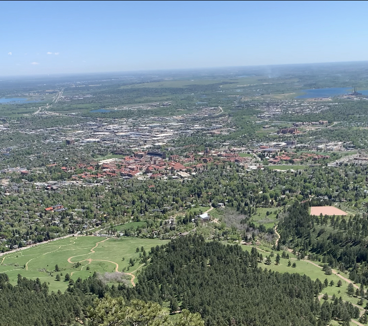 The city of Boulder, Colorado from above. Red brick buildings surrounded by green forests. 