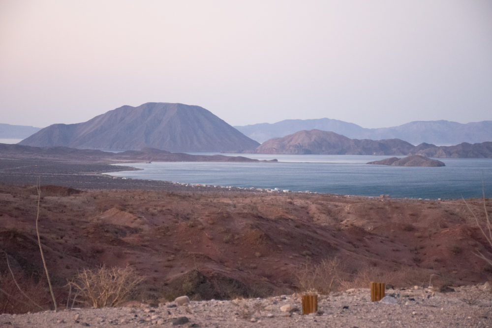 Blue lagoon in the midst of the desert with pinkish mountains in the background. 