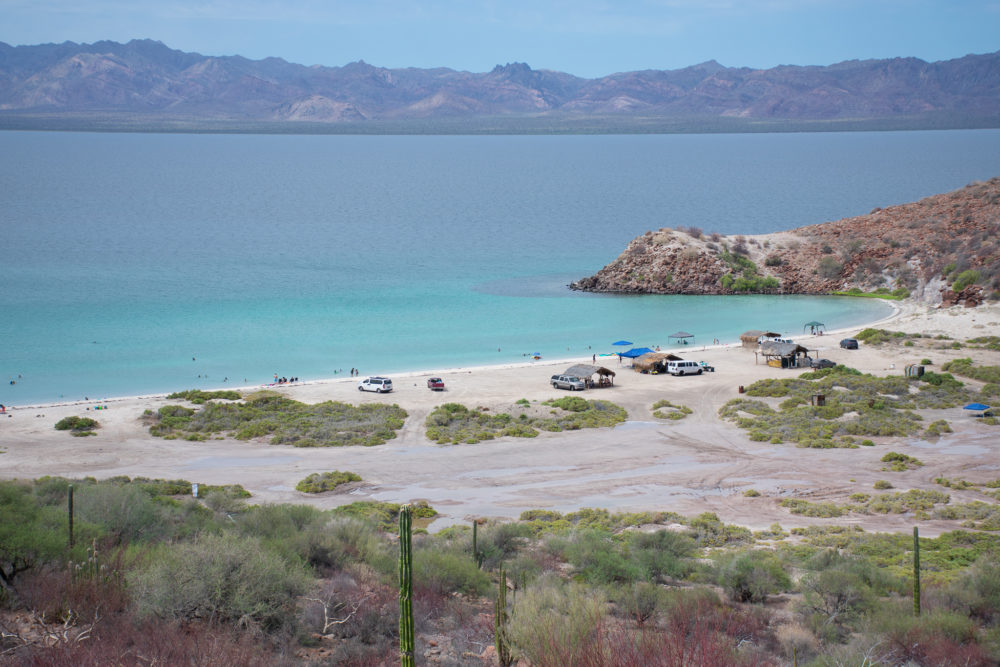 A circular bay with some car campers on the sand. Water is bright and tropical. 