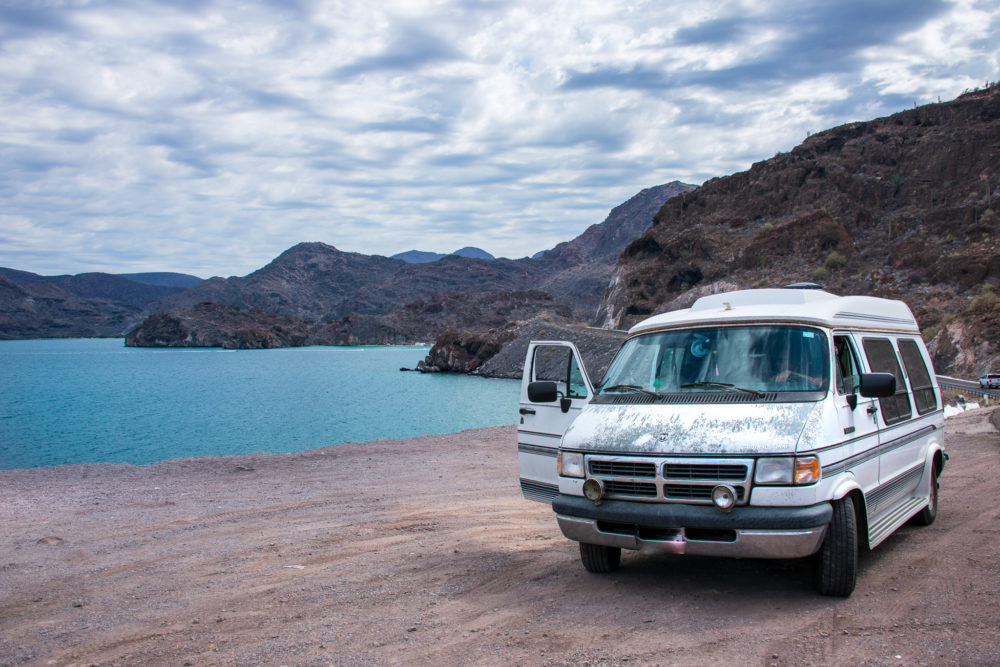 Van with peeling paint and lots. of windows parked at an overlook to turquoise ocean water.  Things we love about our campervan