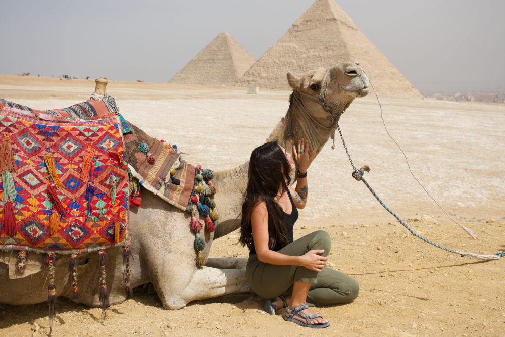 Woman petting a camel in Giza with pyramids in the background. 