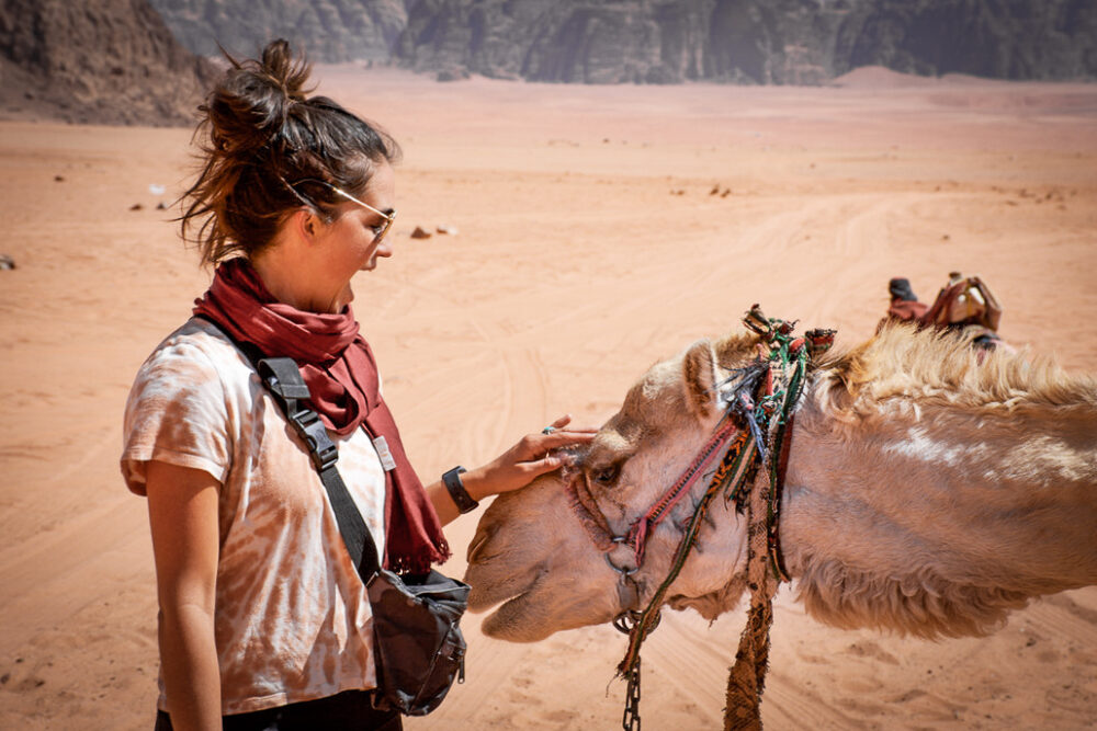 woman petting a camel in the desert. Budget travel guide to Jordan 