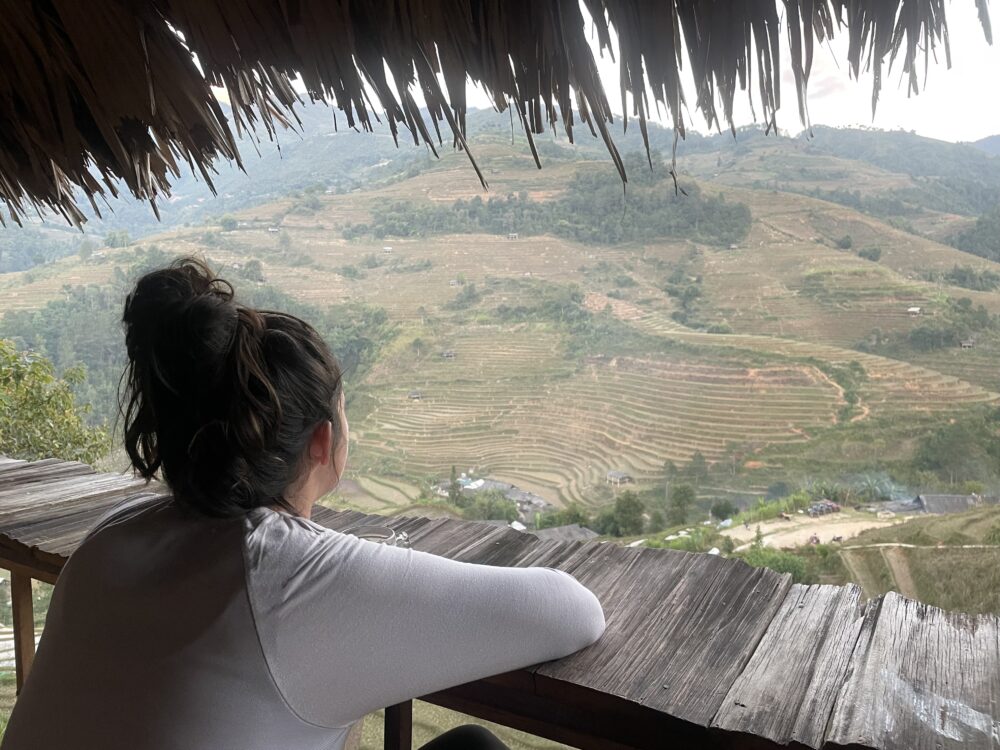 Woman looking out over the rice terraces from a wood balcony. 