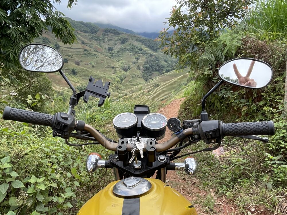 Gold motorbike with a view of the green rice terraces between the handle bars. 