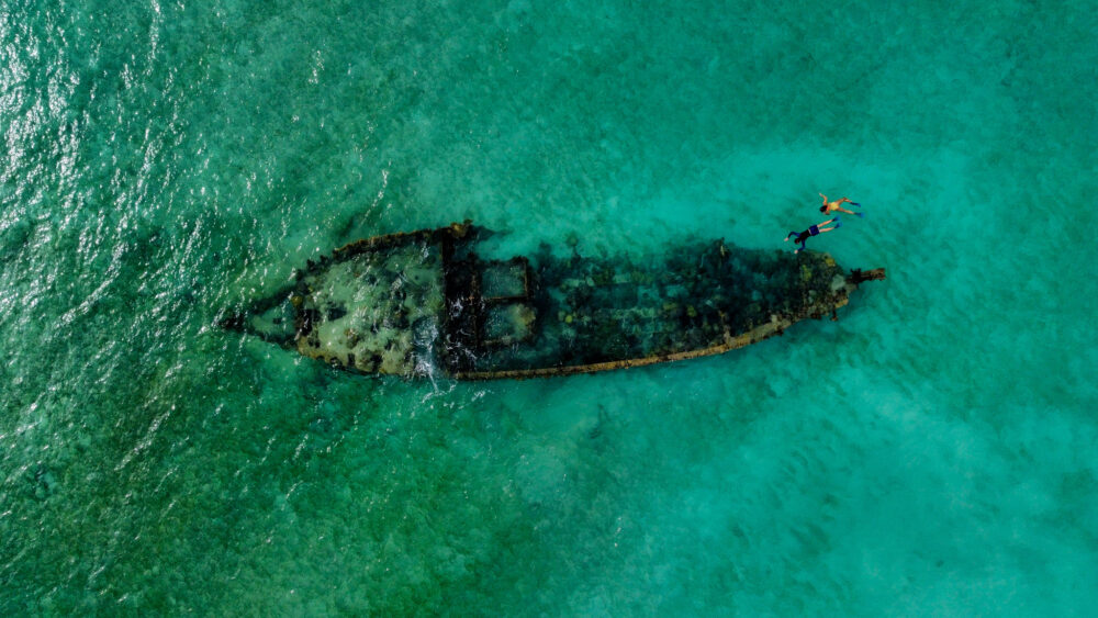 View of a shipwreck from above with two snorkelers floating above it. 