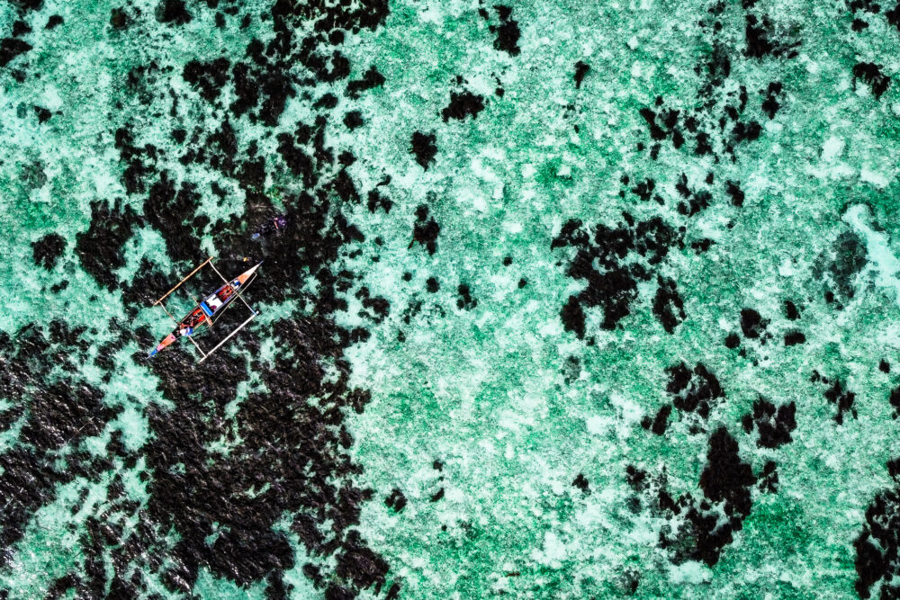 A small red and blue traditional Filipino boat from above in the blue water. 