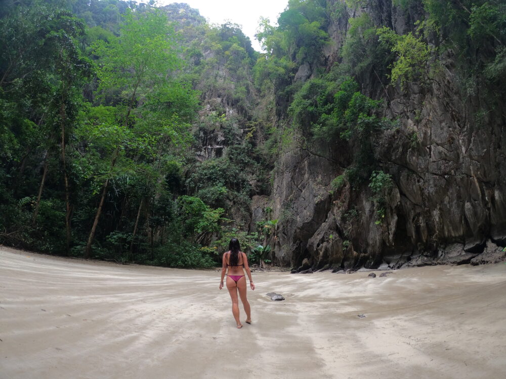 Woman in a bikini standing on a beach inside a limestone mountain. 