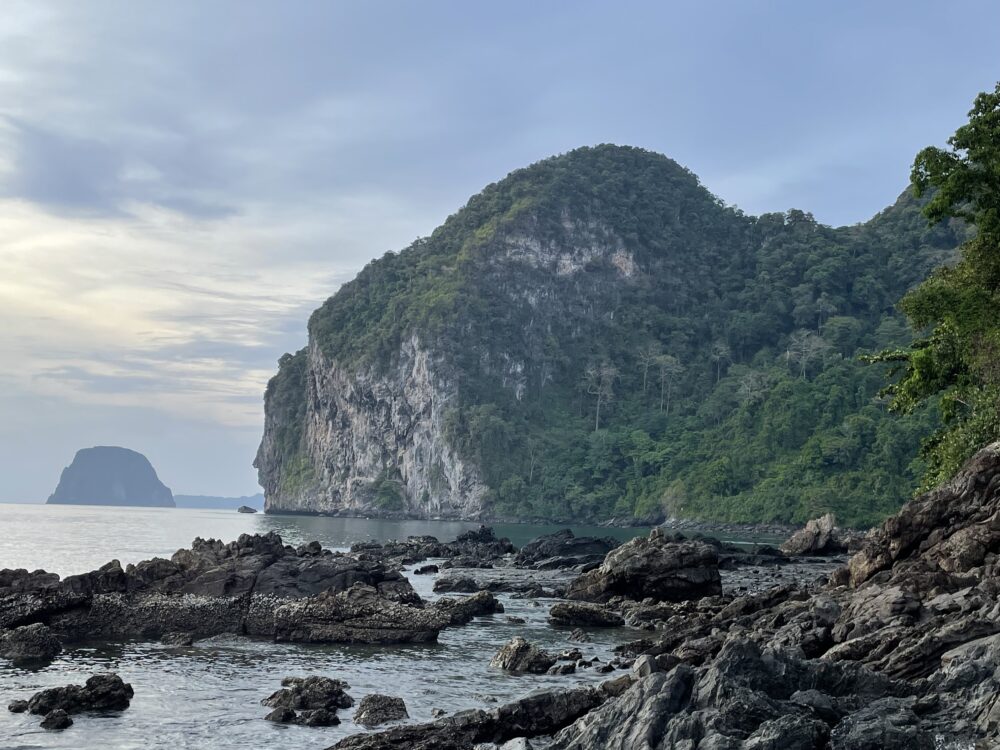 Rocky shoreline of the beach in Koh Mook with a rock that is shaped like buddha head. 