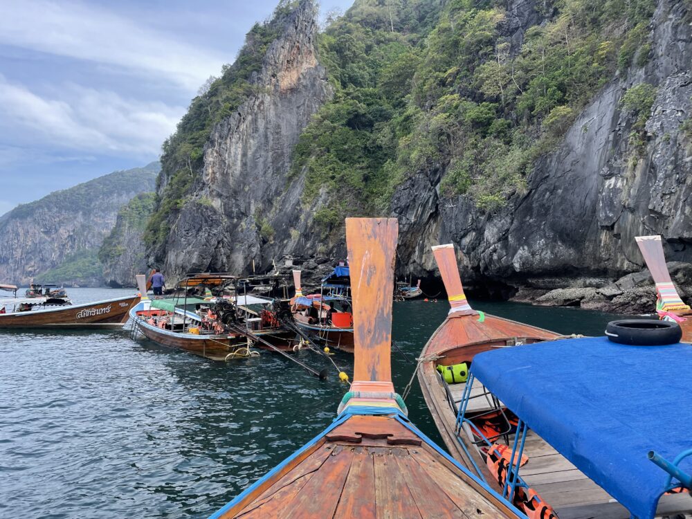 Lots of Thai longtail boats around a cave in the water. 