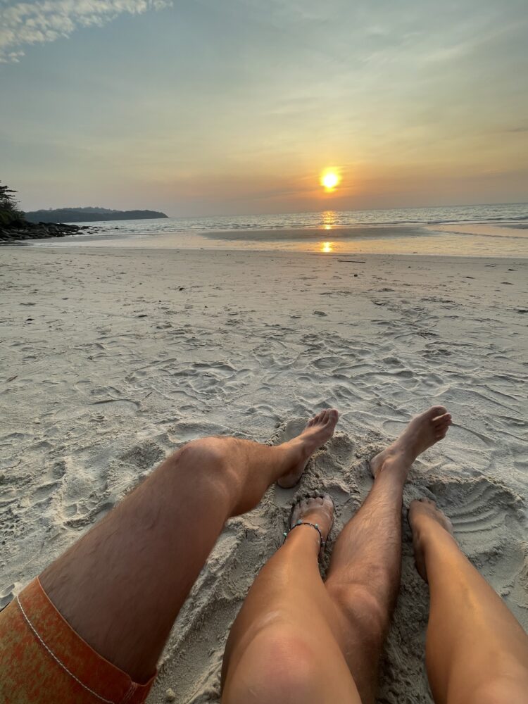 a couple of legs on a beach enjoying the sunset. 