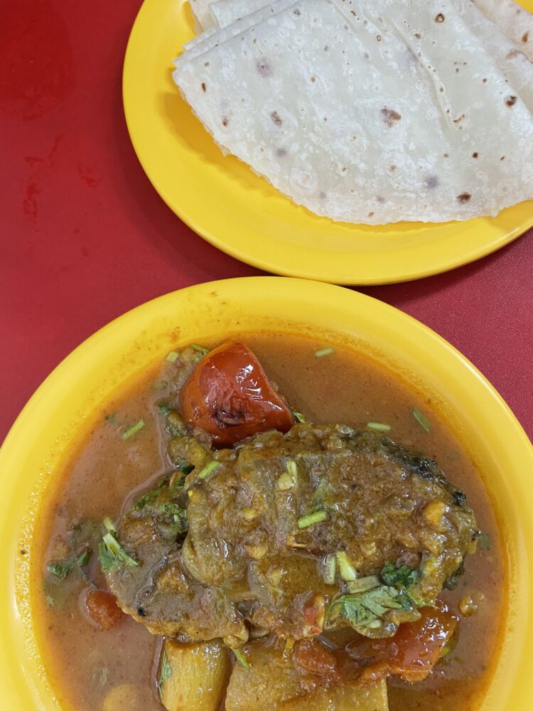 fish curry on a yellow plate with roti on the side. 