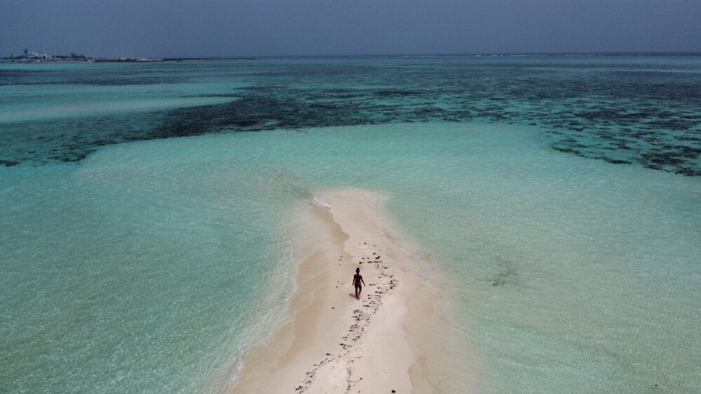 woman standing on a sand bank in the Maldives surrounded by ocean. 