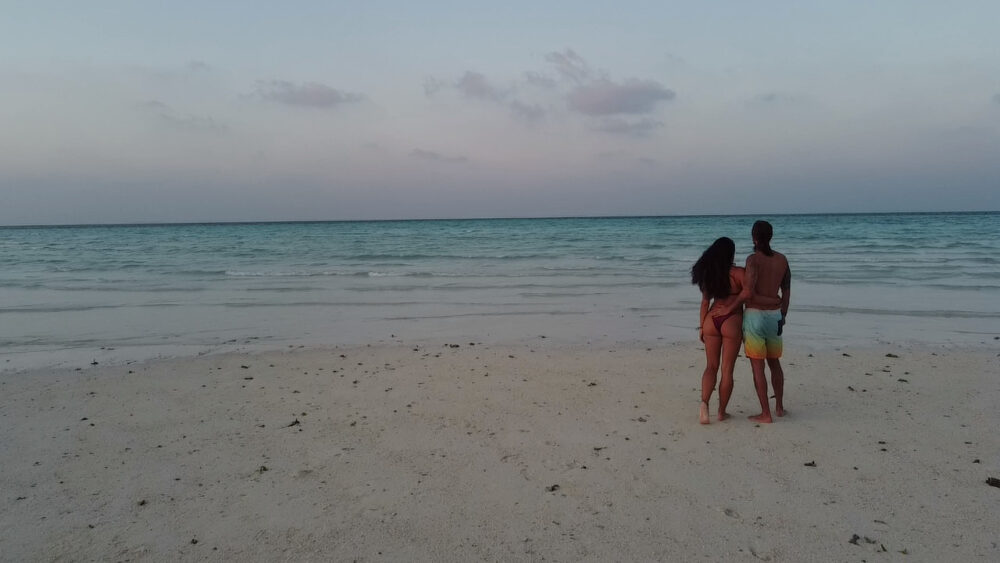 Couple standing on a sand bar in the Maldives at sunset. 
