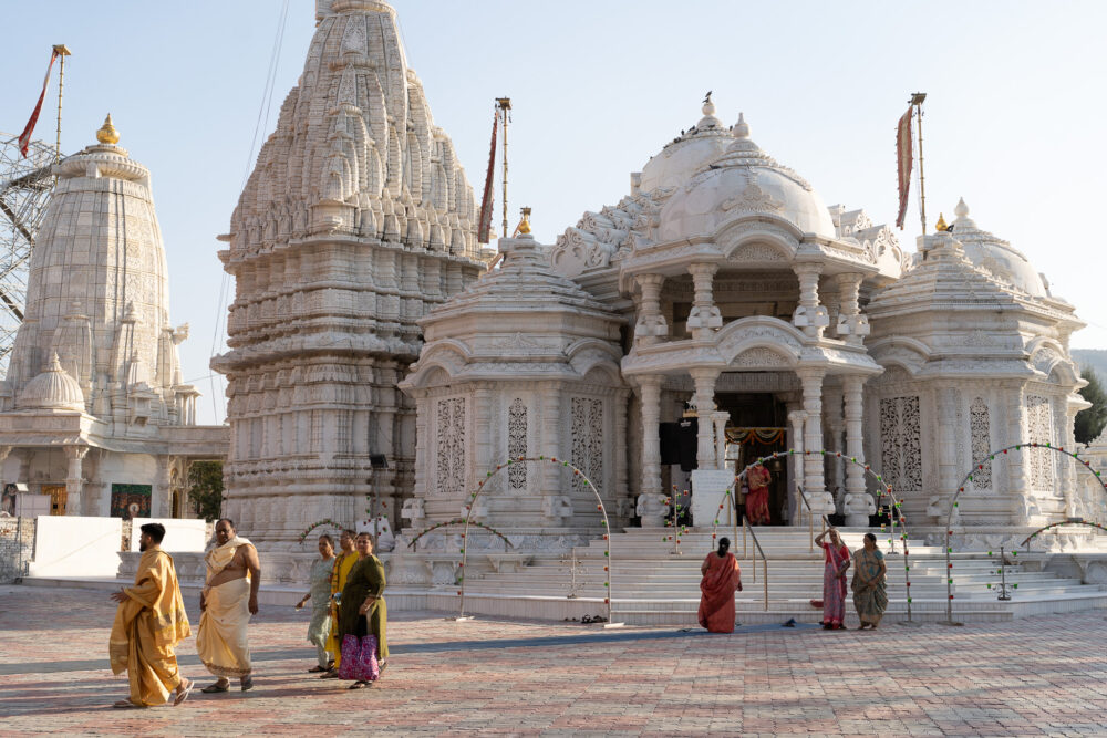 Big white temples with lots of people outside in colorful sari. 