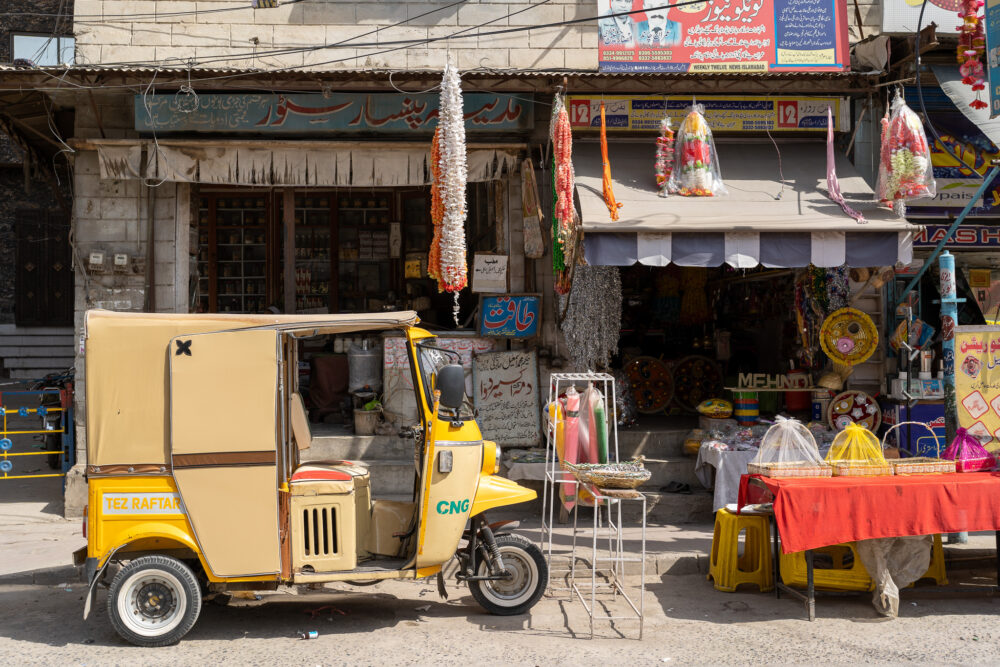 A yellow rickshaw on the side of the road in Lahore on a street with eclectic shops in the background. Wagah Border Crossing 