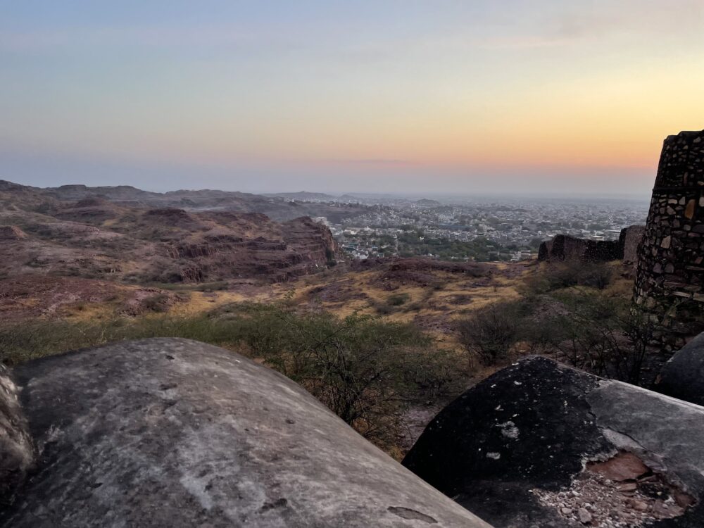 Sunrise colors in the sky over a large scrubland landscape and an ancient wall. 