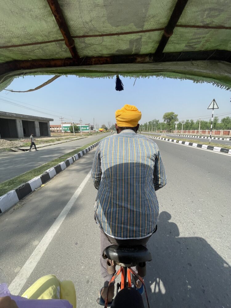 A man in a yellow headscarf driving a bicycle rickshaw down the road at the Wagah Border Crossing 