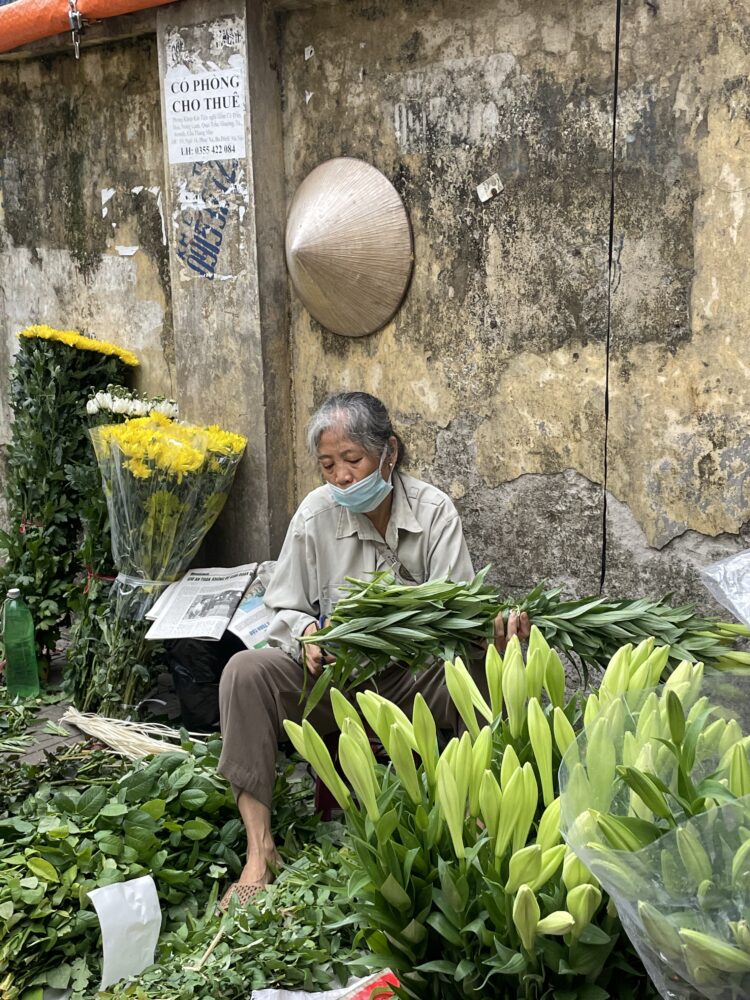 A woman sitting on the side of the road cutting fresh flowers into bouquets. 