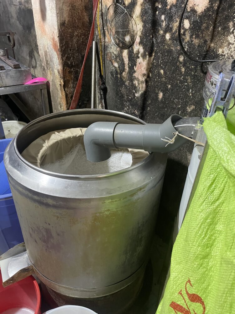 A large metal container where soy milk is being strained. 