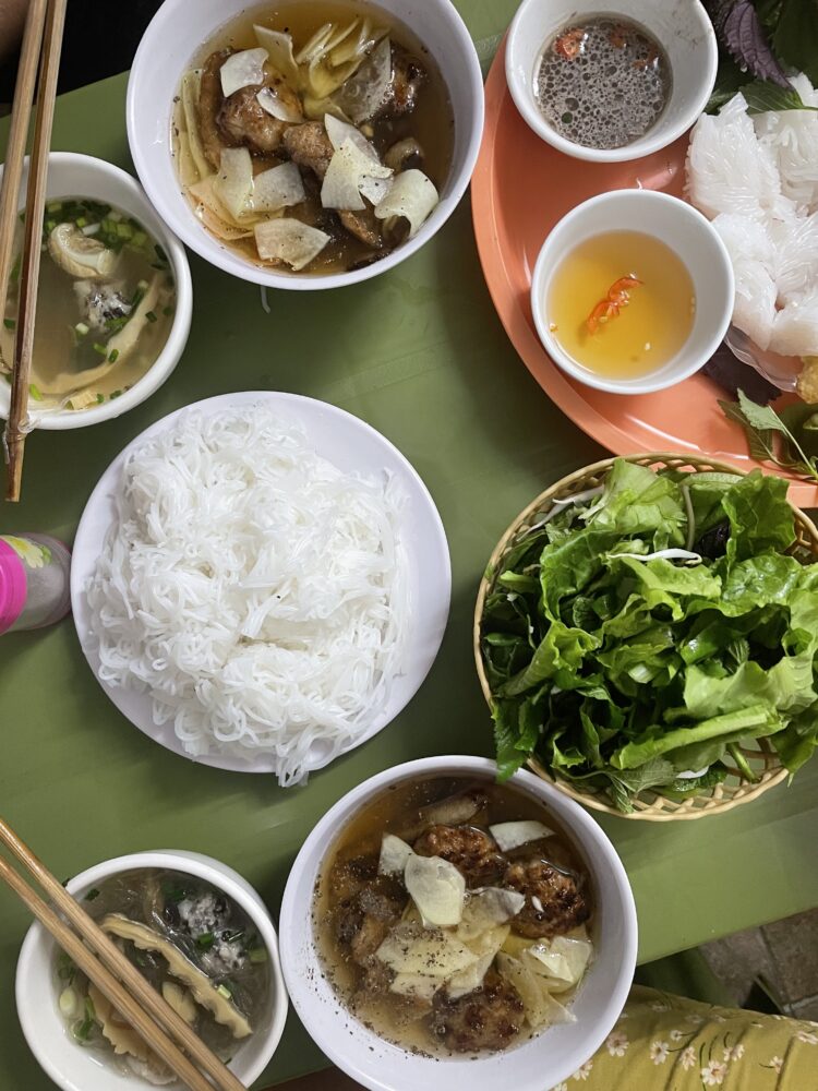 An array of noodles, bun cha, and greens served on a table. 