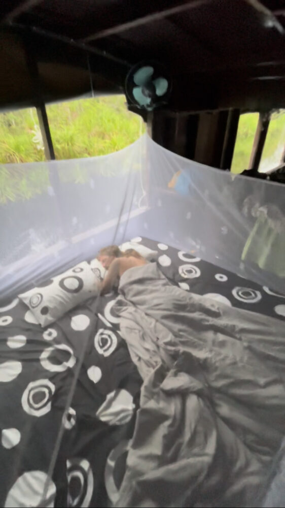 A man sleeping in a bed with a large mosquito net over it on the trekking tour. 