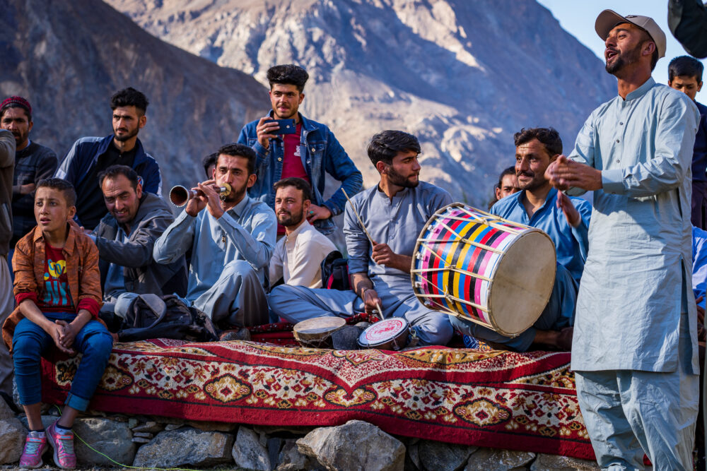 Men playing musical instruments outside on top of colorful carpets. 