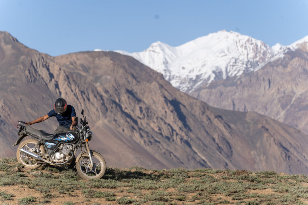 Man setting up his motorcycle with mountains in the background 