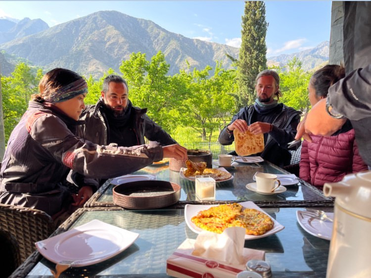 A group of people eat breakfast outside at a table. 