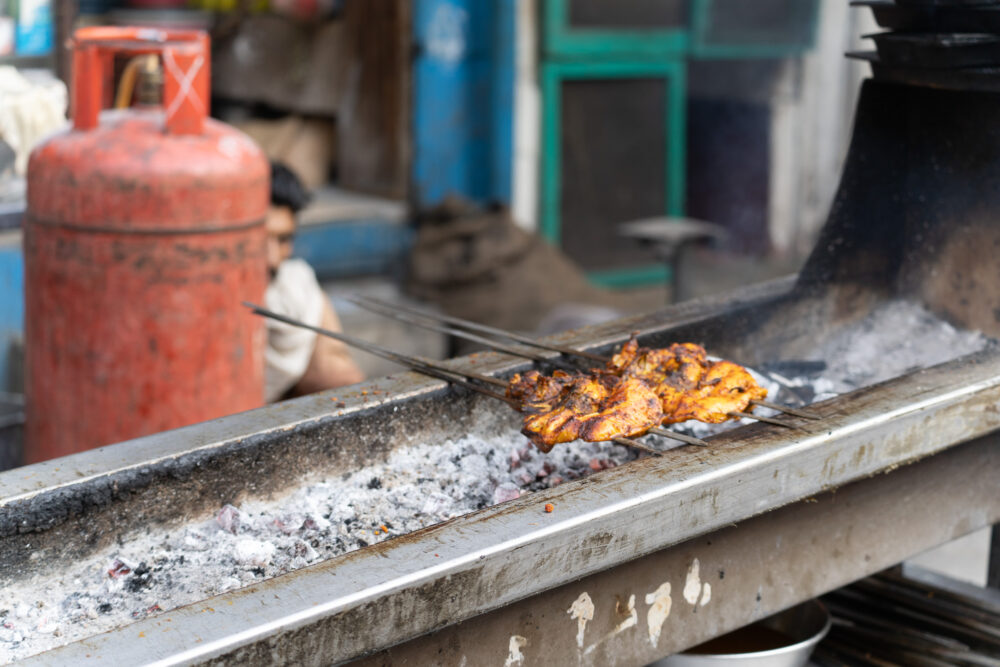 Chicken being grilled over a small charcoal grill. 