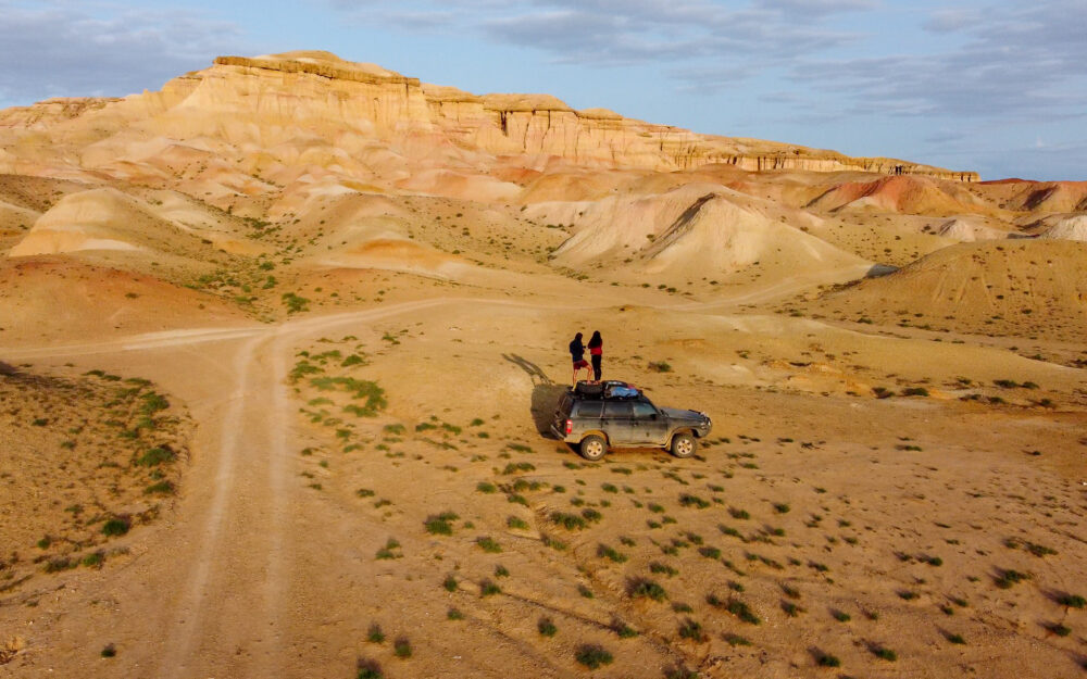 Couple standing on a car in the desert in front of some cool rock formations 