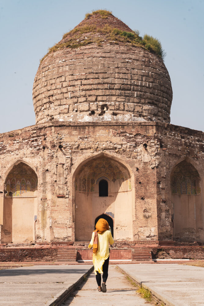 Woman in a headscarf walking toward an ancient crumbling dome. 