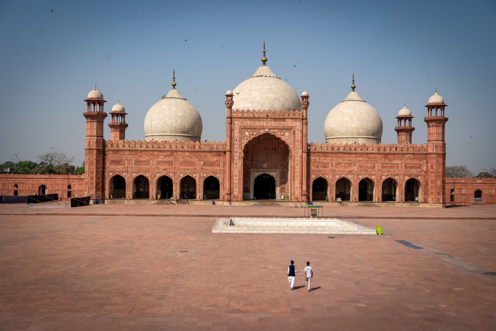 red mosque with white domes and two men walking toward it 